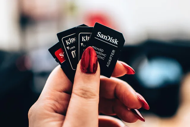A close-up image of a woman's hand holding multiple microSD memory cards with red nails. Checking storage and history limits