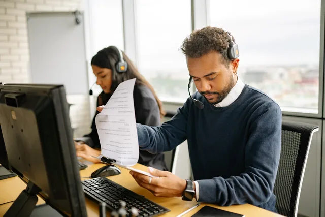Call center agents with headsets working in a modern office setting, reviewing documents. Comparing public and agent-only knowledge bases