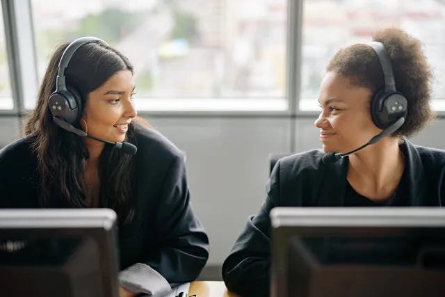 Two smiling female call center agents with headsets engaging in teamwork. Estimating AI feature charges from actual case volume